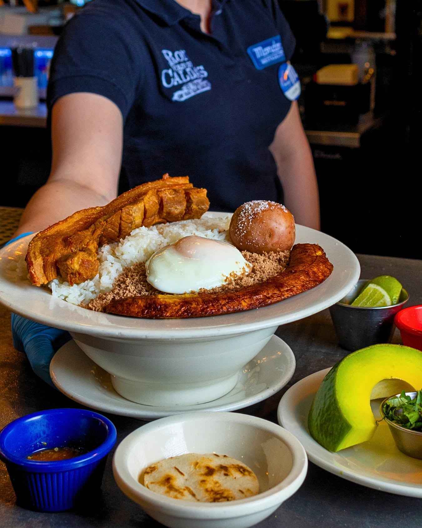 Server presenting a bandeja paisa with chicharrón, egg and plantain
